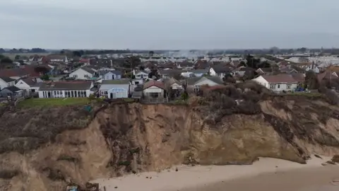 Qays Najm/BBC A drone image of a sandy cliff edge, with a line of chalet properties just a few feet from the cliff edge.