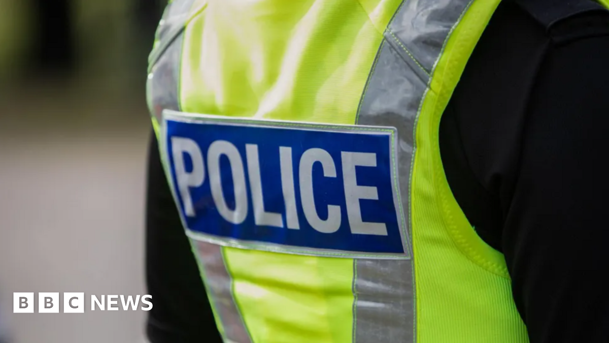 The back of a police officer in a yellow hi-vis jacket with the word "police" on it