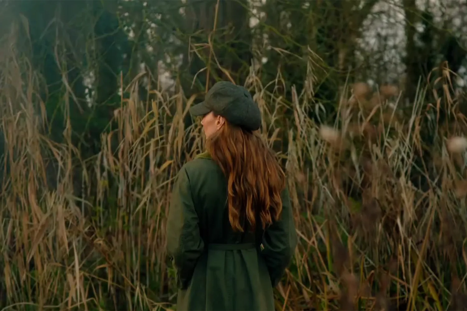 Princess Kate wearing a green coat standing with her back to the camera in front of tall grass