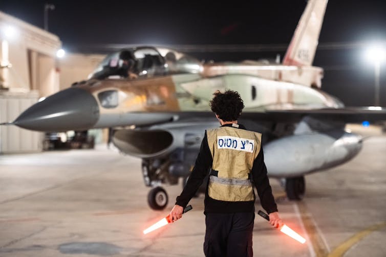 A fighter jet taxiing behind a person holding lights.