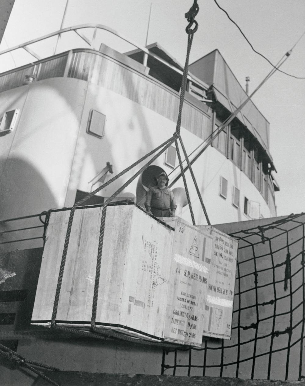 Ropes hoist large boxes aboard a ship.