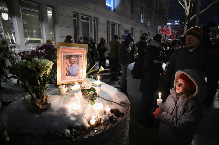 A child holds a candle next to a makeshift memorial for Alex Pretti outside the US Department of Veteran Affairs in Washington DC, on January 28, 2026.