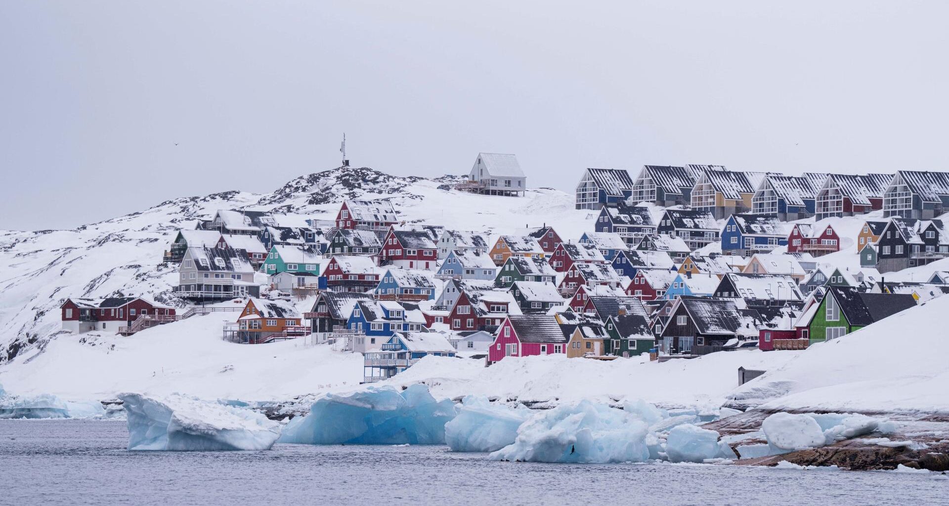 Sschneebedeckte Häuser auf einer Landzunge vom Meer aus gesehen.