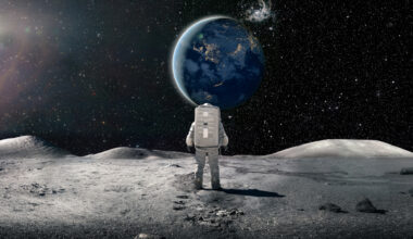 A single astronaut viewed from behind, standing and looking at the sun rising over a distant plant earth surrounded by distant stars and galaxies. The astronaut is wearing a conventional white spacesuit with backpack. Earth image from NASA: https://eoimages.gsfc.nasa.gov/images/imagerecords/79000/79790/city_lights_asia_night_8k.tif