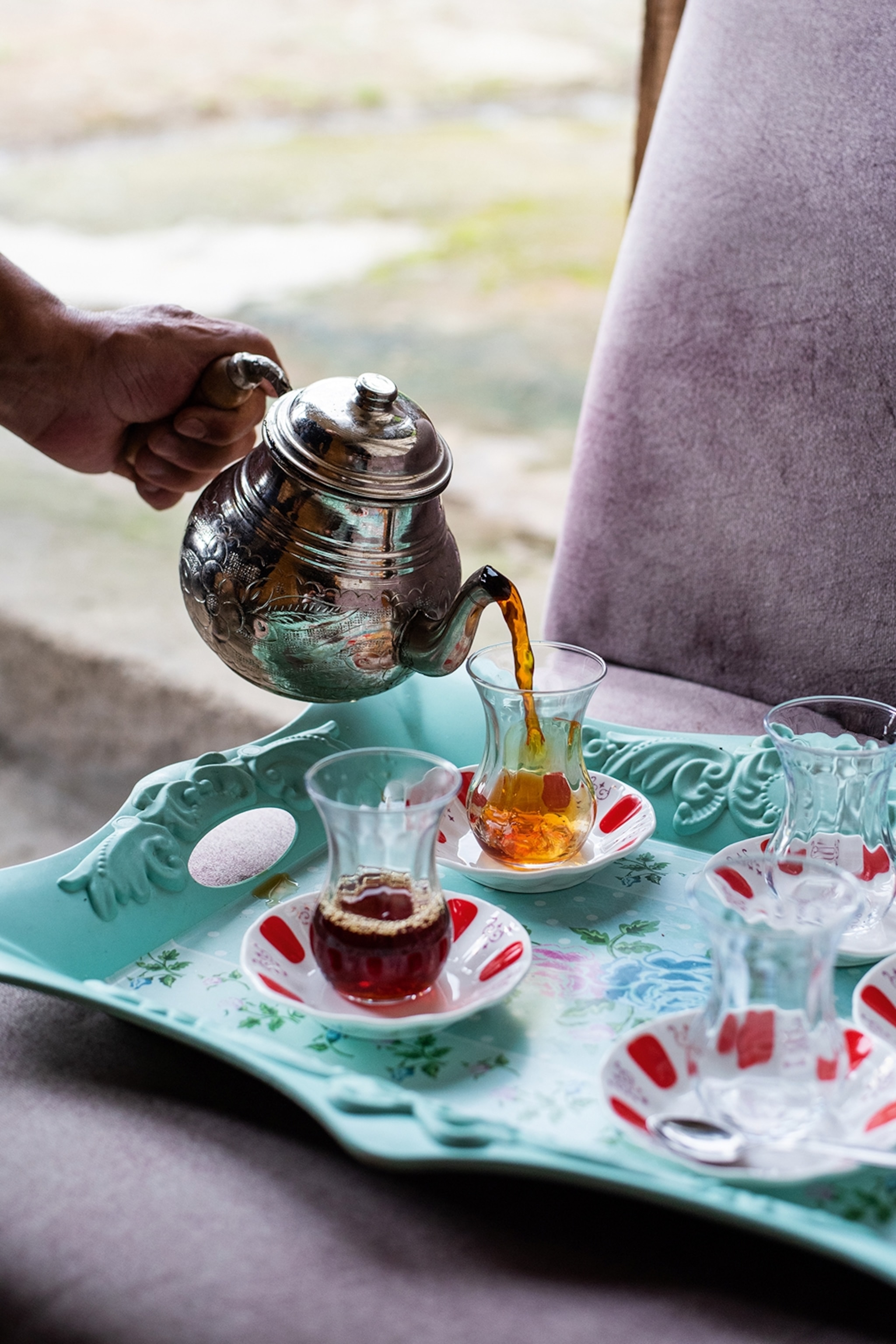 A colourful tea tray with traditional tulip-shaped glasses as someone is pouring tea into them from a silver tea pot.