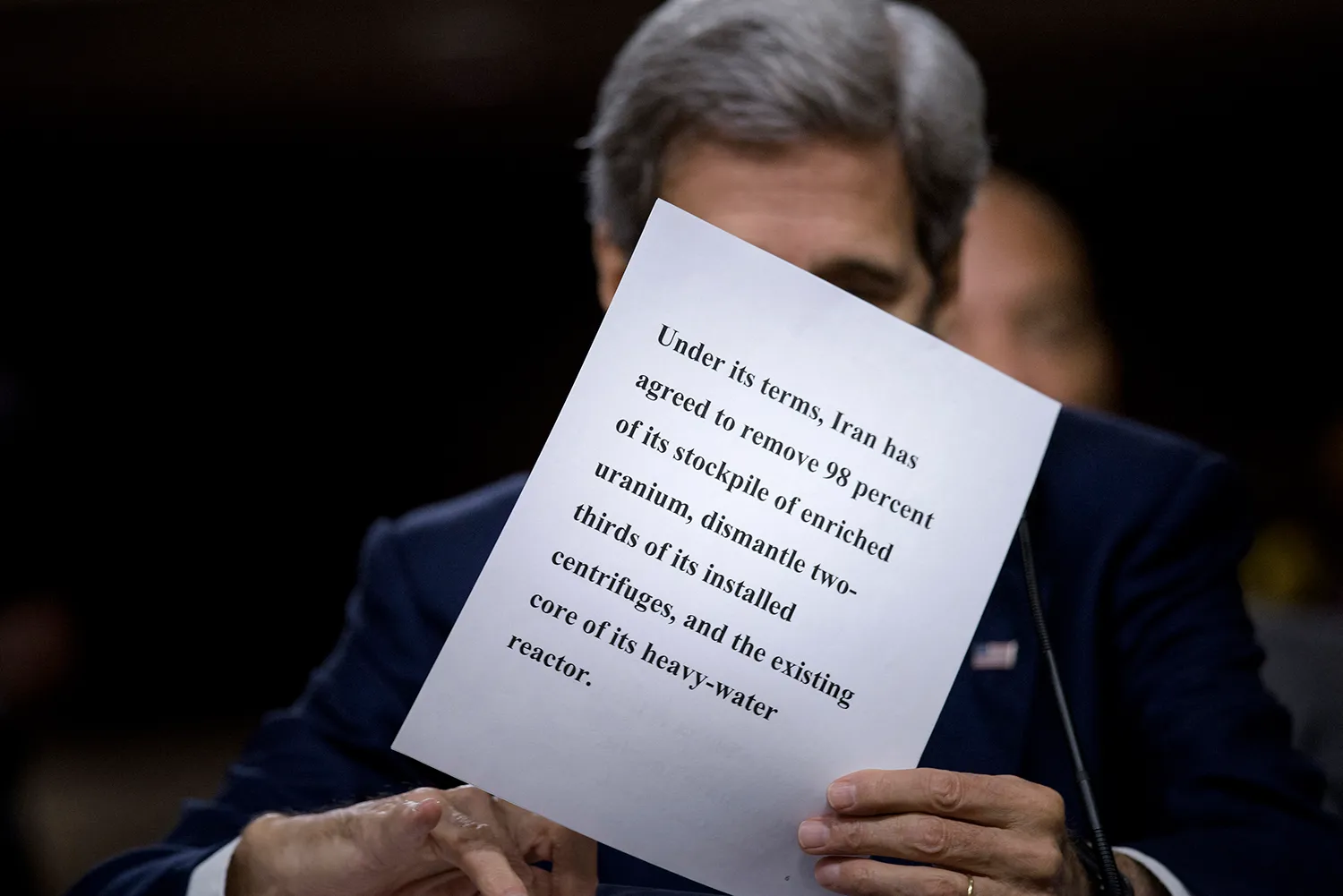 A man with gray is partially obscured by a paper with words about the Iran nuclear deal on it.