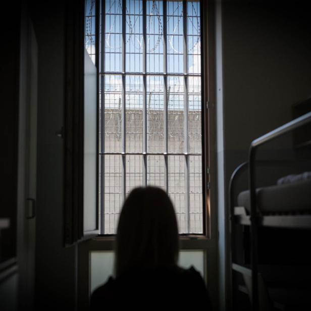 Eine Person blickt aus einem Fenster mit Gittern und Stacheldraht.