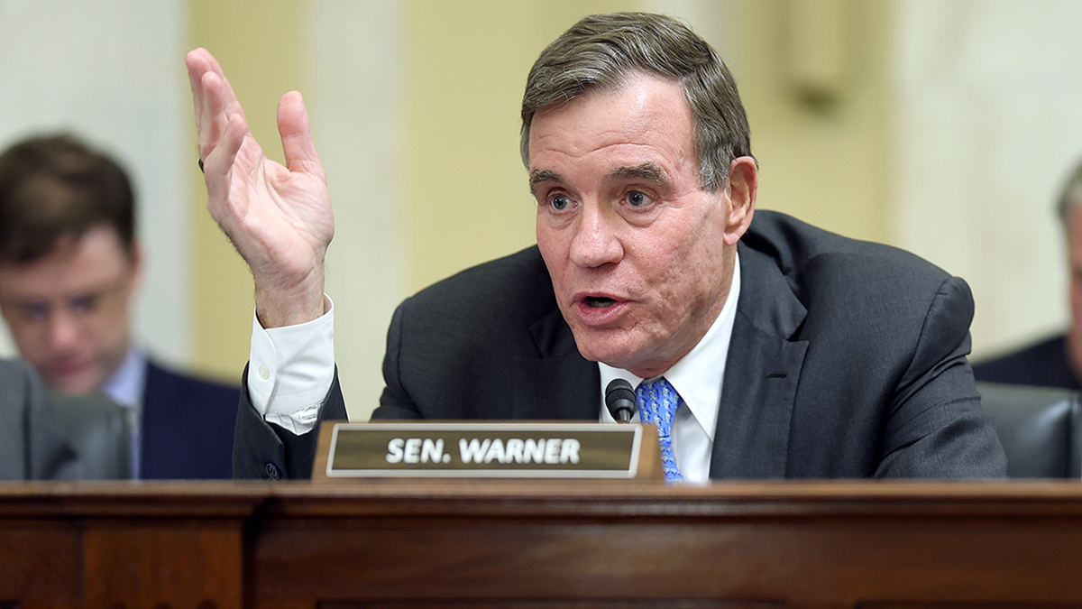 Mark Warner raises his palm during a hearing