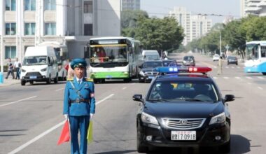 North Korean traffic police officer directing traffic on wide street in Pyongyang with police car, buses, and vehicles. driving