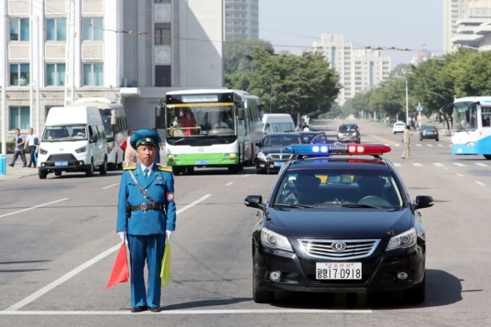 North Korean traffic police officer directing traffic on wide street in Pyongyang with police car, buses, and vehicles. driving