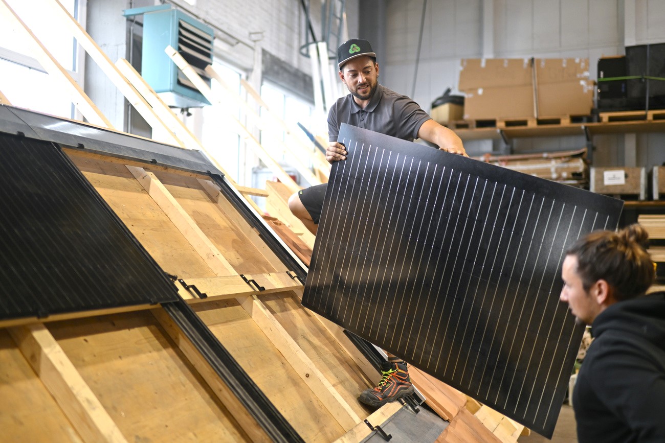 Two apprentices install a solar panel on a wooden roof.