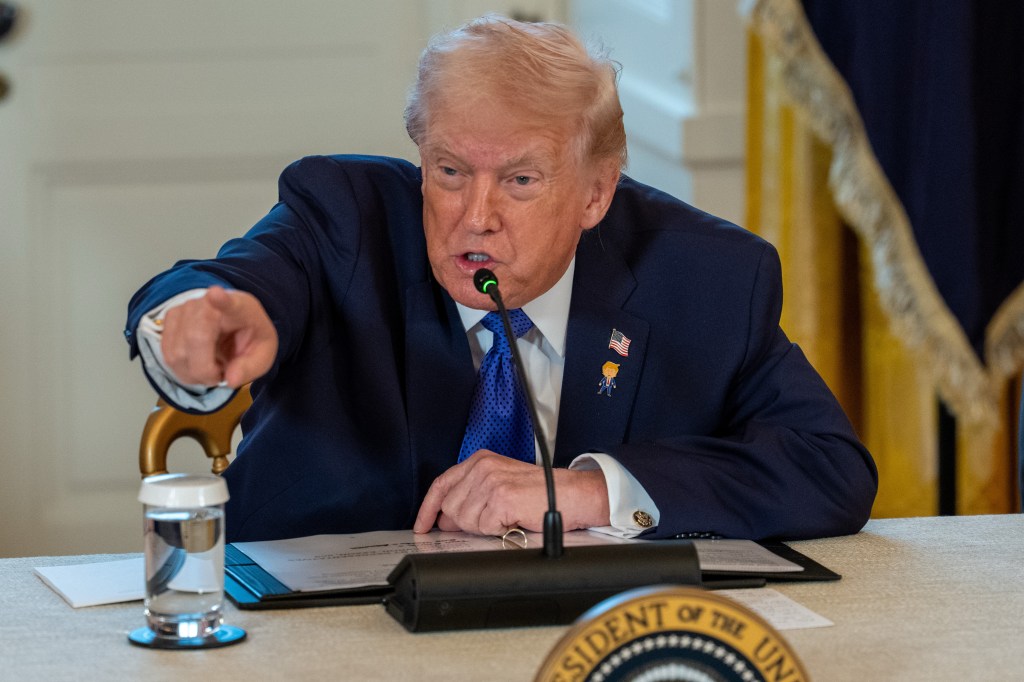 Donald Trump pointing while speaking at a microphone.