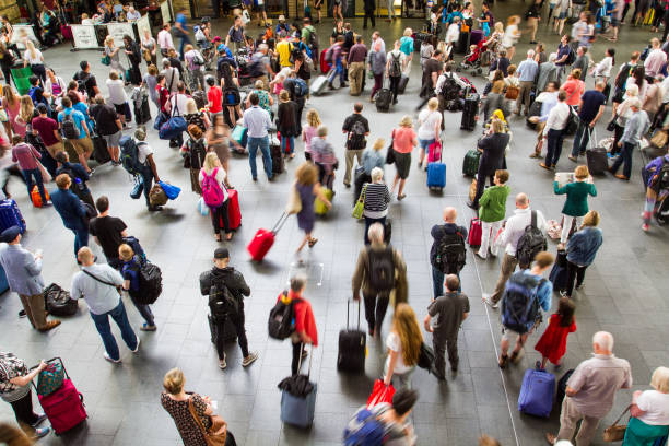 Crowd of travelers moves through a busy transport hub, many pulling rolling suitcases across the open floor.