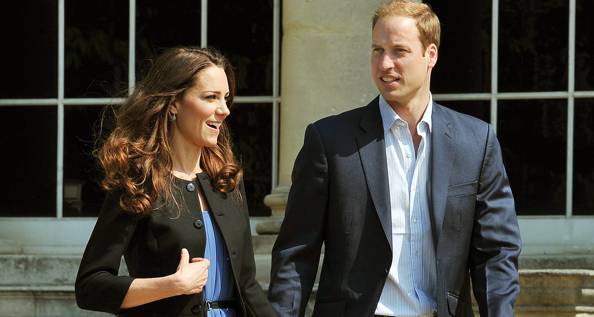 Princess Kate wearing a black blazer and blue dress holding walking next to Prince William