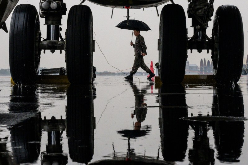 A soldier uses an umbrella to shield himself from the rain as he walks past the front wheels of a B-52H strategic bomber parked at a South Korean Air Force base at Cheongju International Airport on Oct. 19, 2023.
