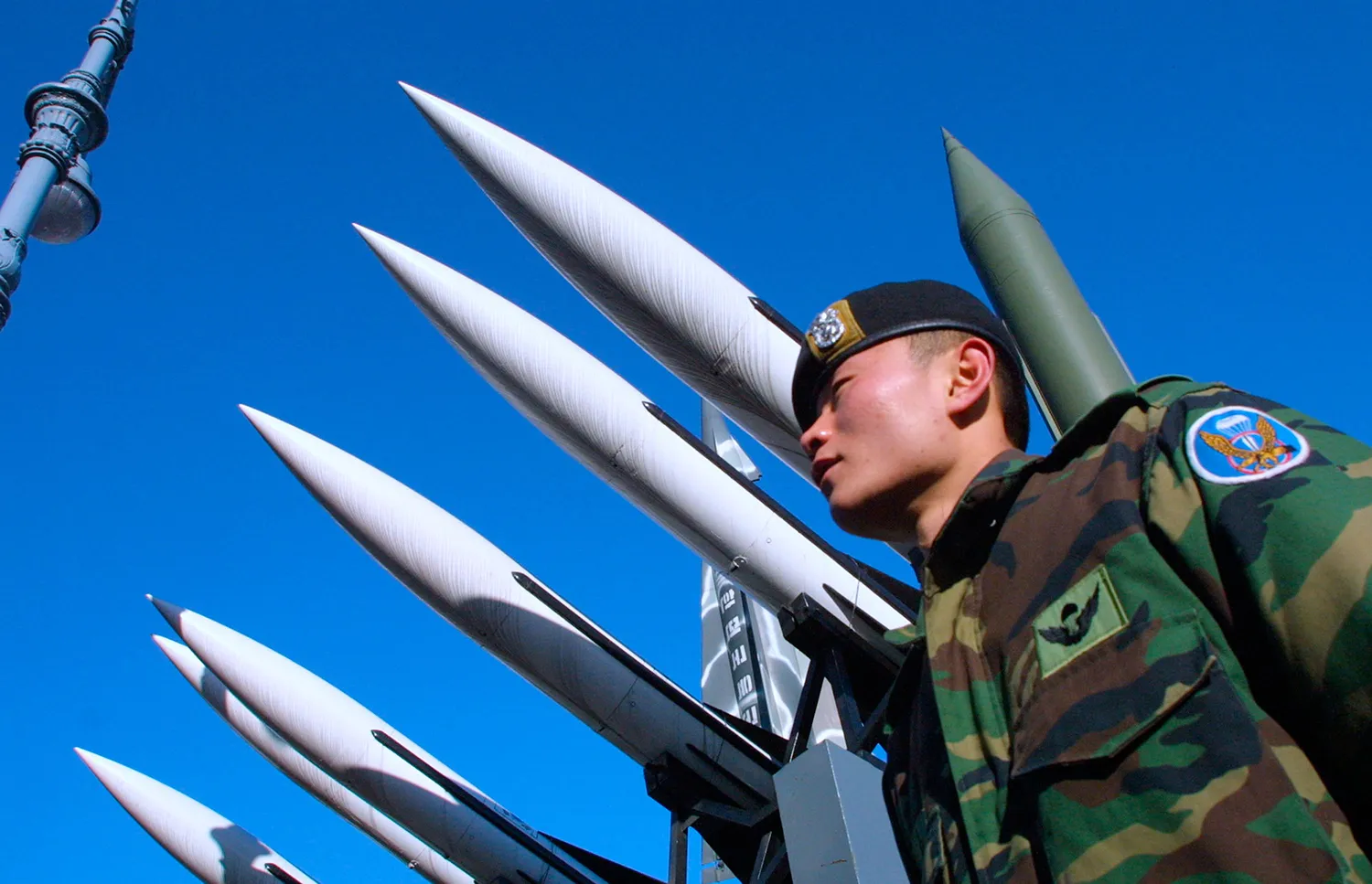 A soldier stands in front of a monument made of missiles.