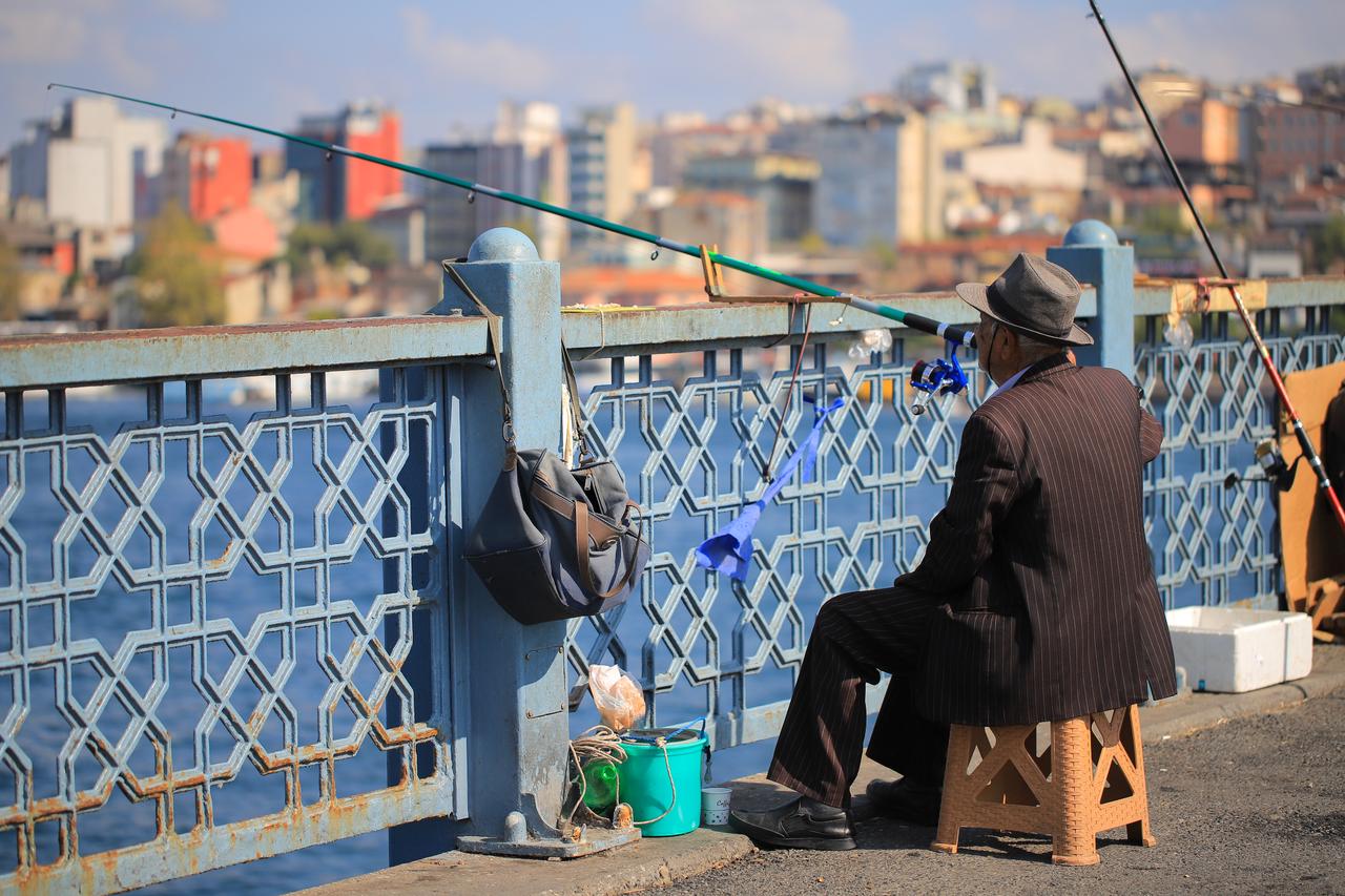 An old man catching a fish on a bridge, Istanbul, Türkiye. (Adobe Stock Photo)