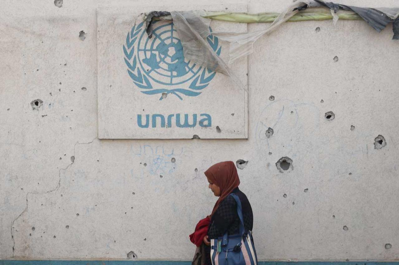 A Palestinian woman walks past a damaged wall bearing the UNRWA logo at a camp for internally displaced people in Rafah in the southern Gaza Strip, May 28, 2024. (AFP Photo)