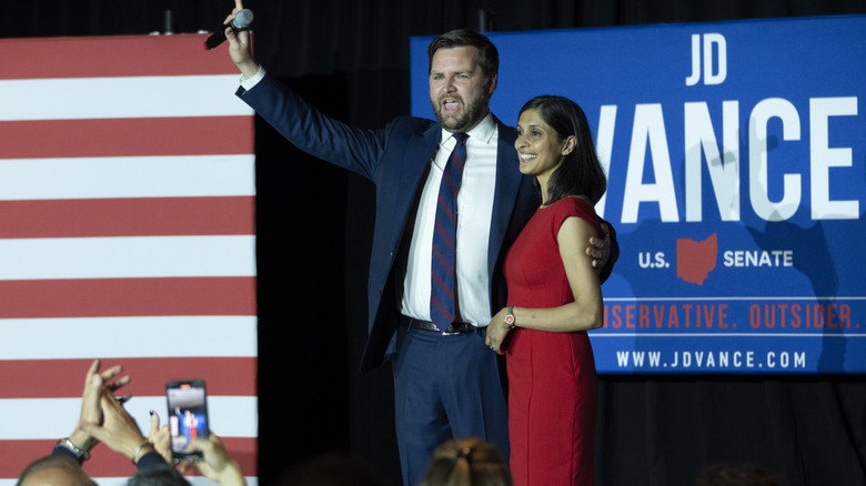 JD Vance waves to a crowd while his other arm is wrapped around a smiling Usha Vance