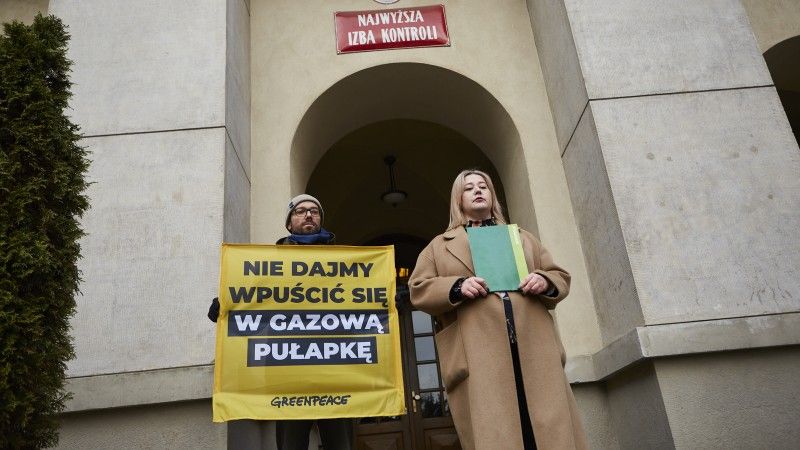 Dwoje działaczy Greenpeace Polska stoją przed Najwyższą Izbą Kontroli z bannerem: Nie dajmy wpuścić się w gazową pułapkę