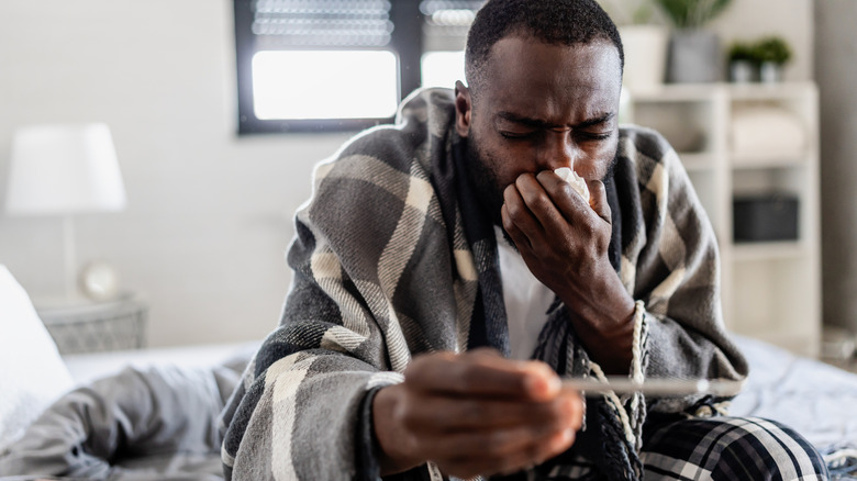 man sick in bedroom while checking thermometer