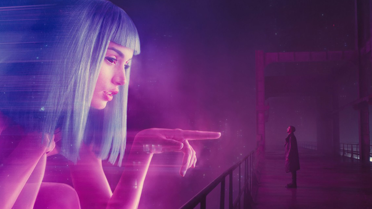 Still from the movie "Blade Runner 2049" Giant AI woman pointing directly at a man wearing a trench coat on a bridge.