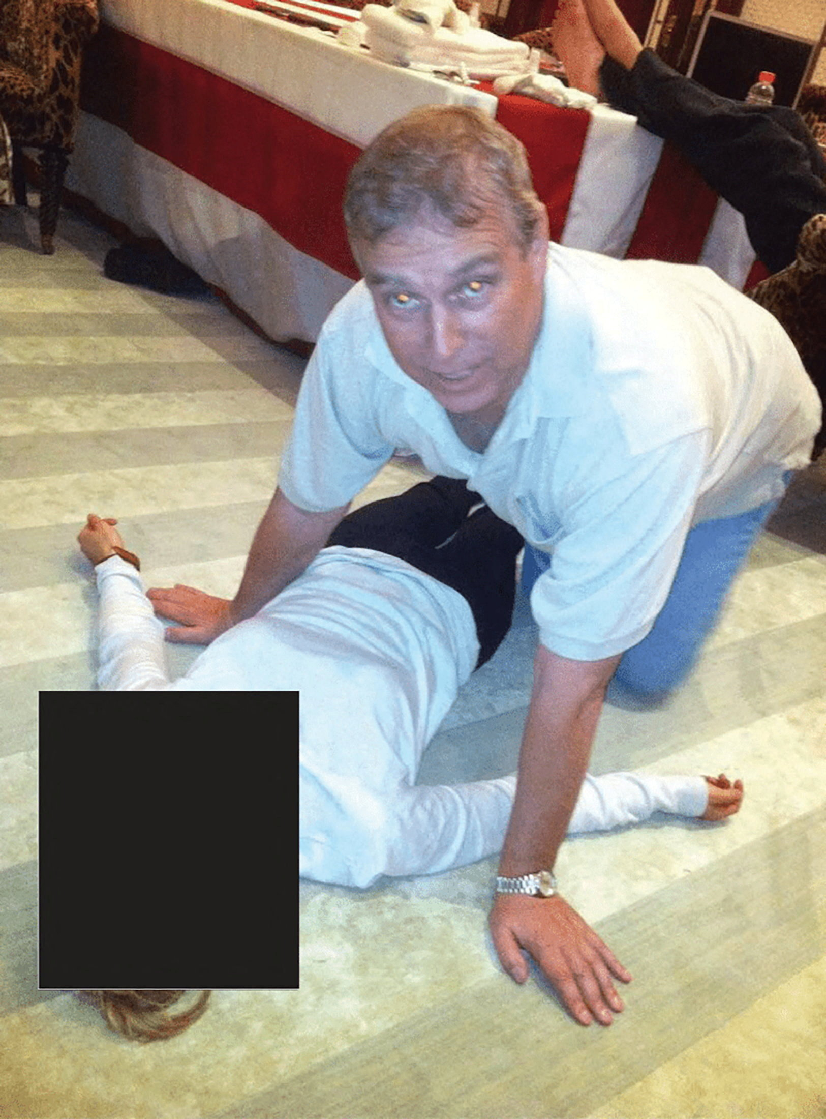 Prince Andrew kneels over a female on the floor, with a black rectangle censoring part of the female figure.