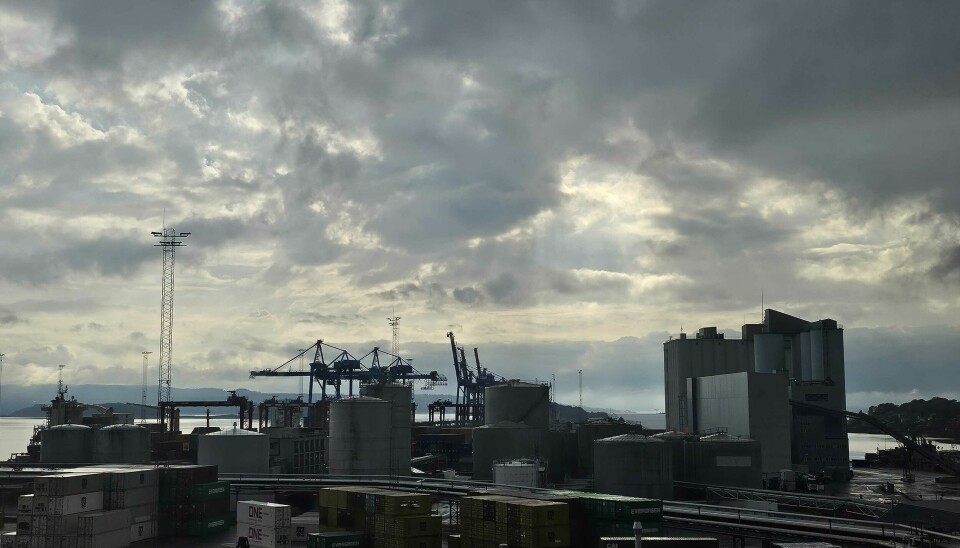 Industrihavn med kraner, lagerbygg og containere under dramatisk skydekke.