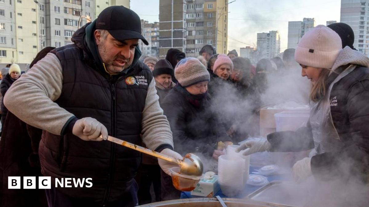 A man pours soup on a pastic cup as a crowd of people wearing winter clothes wait in line