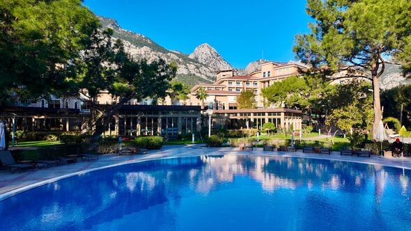 An expansive swimming pool is situated within a well-maintained garden, with lush greenery and a backdrop of majestic mountains An expansive swimming pool is situated within a well-maintained garden, with lush greenery and a backdrop of majestic mountains