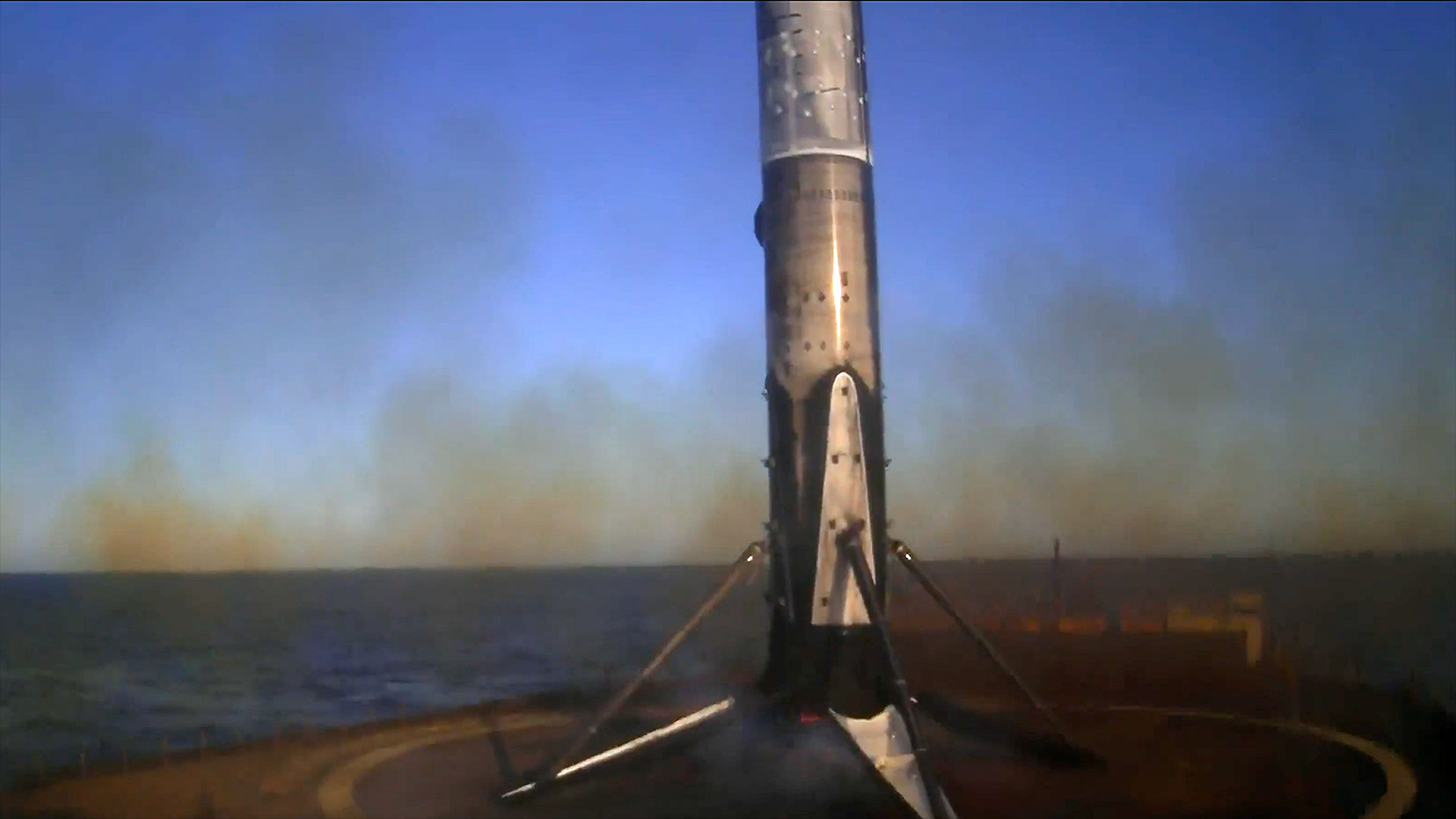 The first stage of an orbital rocket stands on its four landing legs atop an ocean-based droneship following a launch into space.