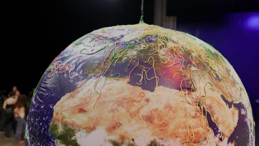 Photo of a large, inflatable globe. It has strands of red, green and yellow pasta stuck to it. 