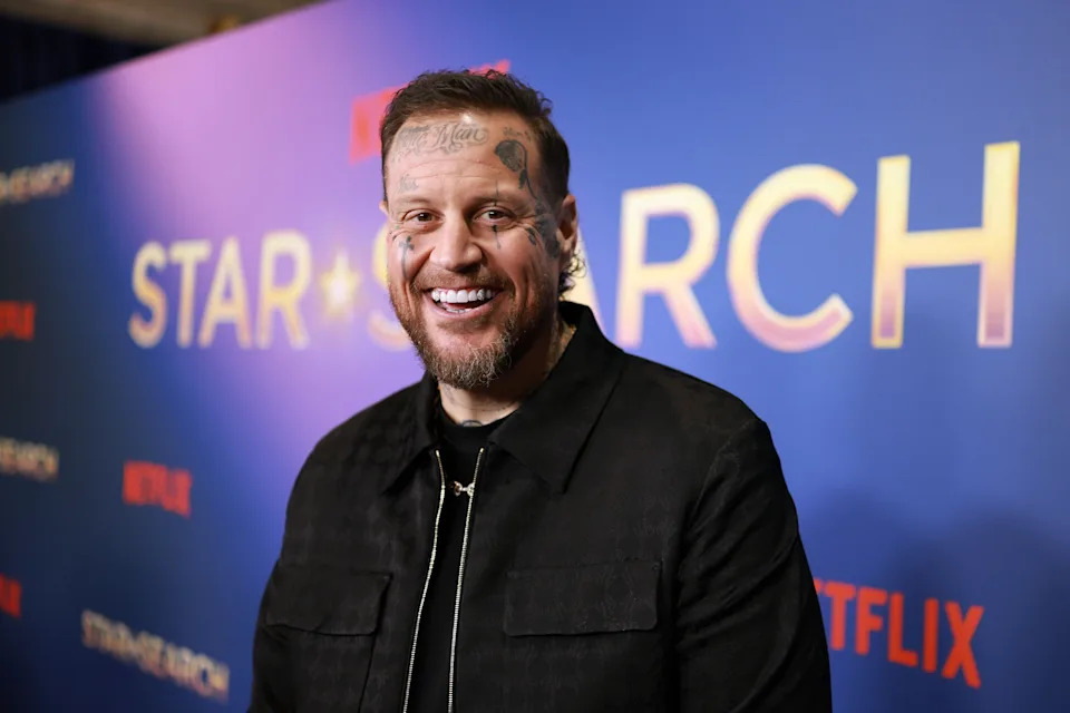 Jelly Roll smiling on the red carpet at a Netflix event, wearing a black jacket. Background features event signage