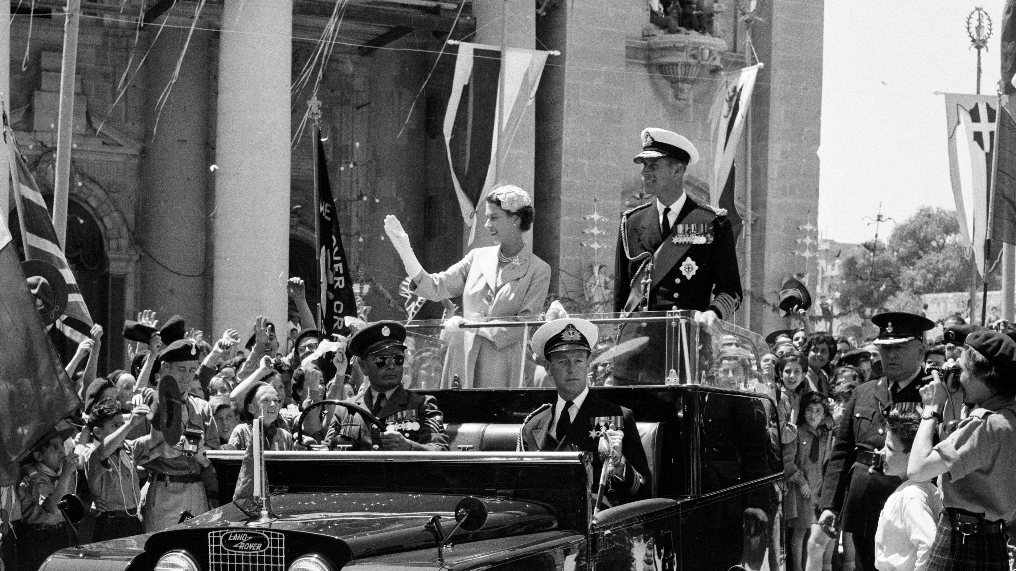 Queen Elizabeth II and Prince Philip wave from an open car to crowds in Malta on the tour of the Commonwealth
