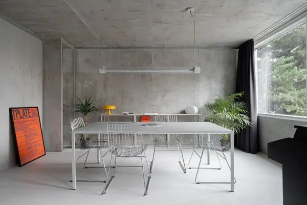 The multifunctional aluminum New Order dining table from Hay is paired with HKLIVING metal wire chairs, a Fatboy Tjoep hanging tube light, and an Artemide Nessino table lamp that adds a welcome pop of color.