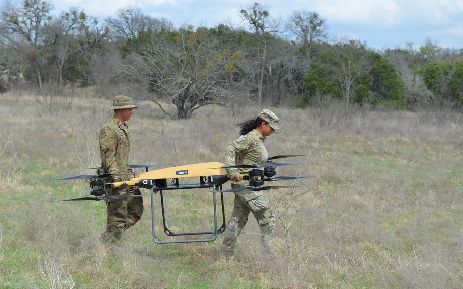 Soldiers carry a drone across a field.