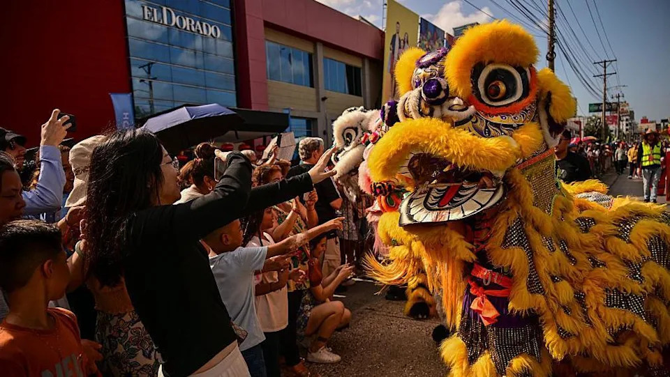 A Chinese New Year dragon costume dances in a crowd on a street in Panama in front of a building that says "El Dorado"