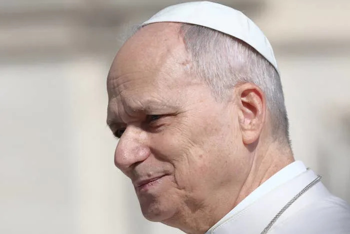 A man wearing a traditional papal white robe and skullcap, outdoors, looking to the side