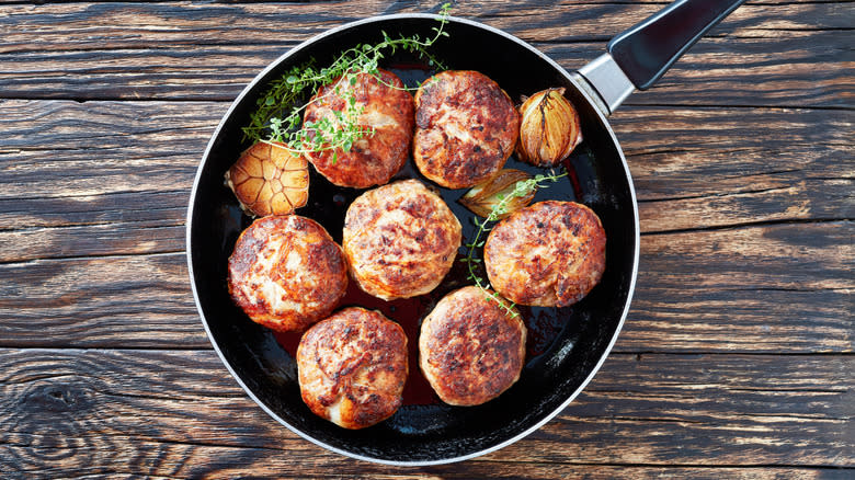 Several Turkey Burgers along with some herbs and garlic in a skillet on a wooden table top