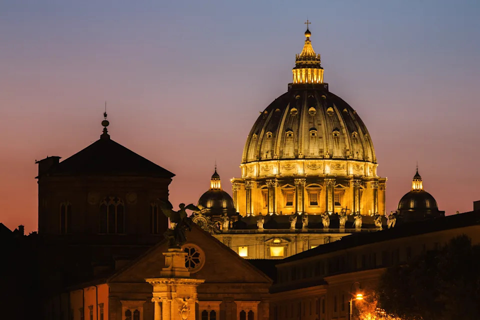 St. Peter's Basilica dome illuminated at dusk, highlighting its architectural grandeur against the evening sky
