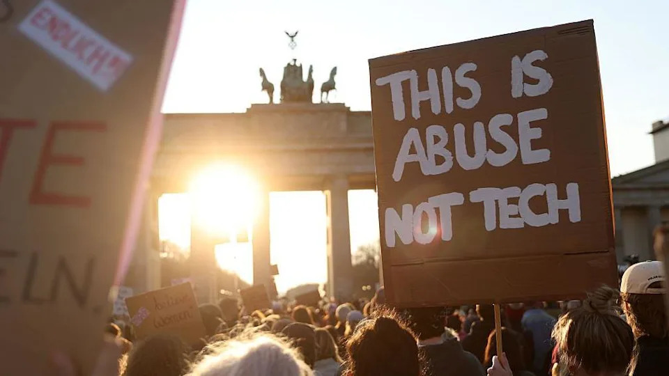 A placard reads "This is abuse not tech" at sunset at the Brandenburg Gate in Berlin