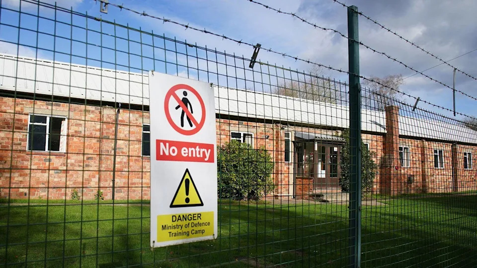 A general view of Crowborough Training Camp, East Sussex. There is a wired fence and a sign, with an area of grass behind it.