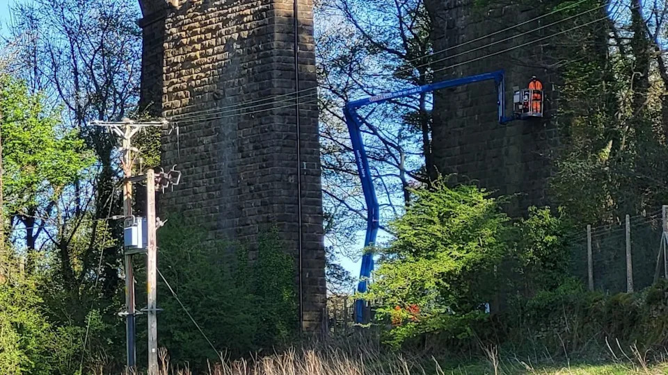 Man in high vis and helmet on crane carrying out works on a stone viaduct 