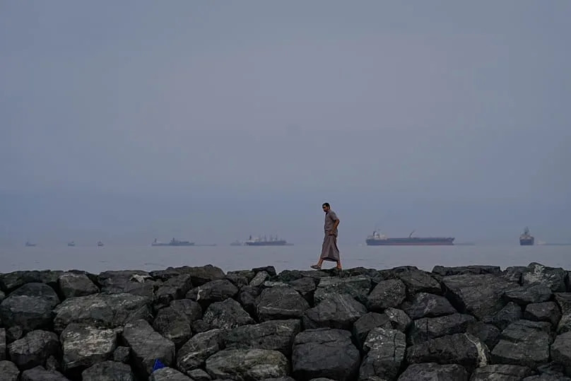 A man walks along the shore as oil tankers and cargo ships line up in the Strait of Hormuz, 11 March, 2026