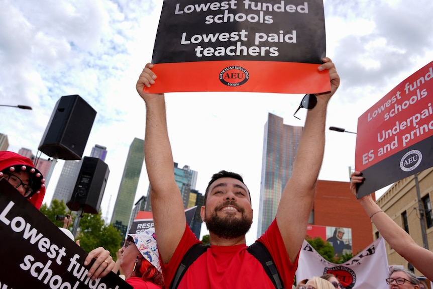 Man holds a placard reading 'lowest funded schools, lowest paid teachers' at a rally in Melbourne.