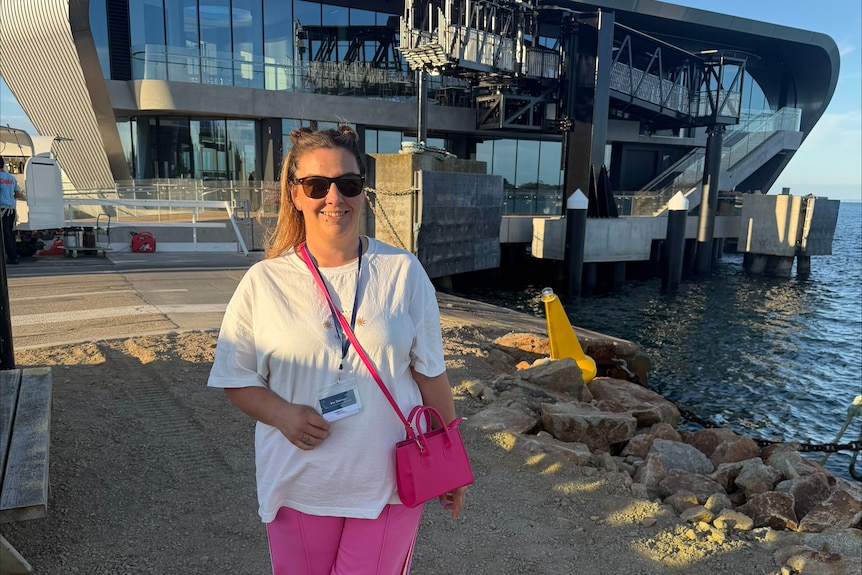 Bec Watson stands in front of a building, on the coast, built out onto the ocean.