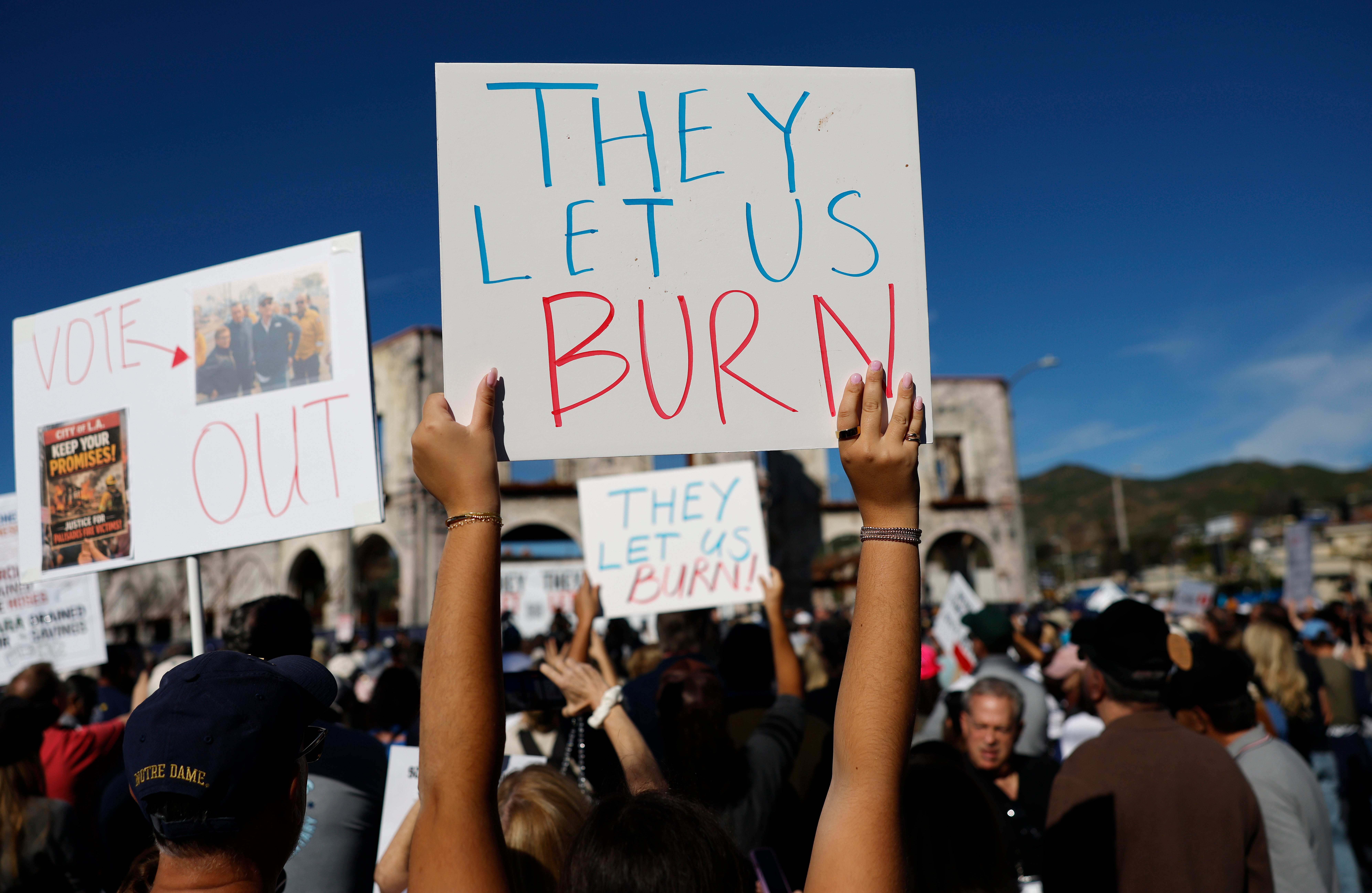 Demonstrators hold signs at the ‘They Let Us Burn!’ rally on the first anniversary of the Palisades Fire