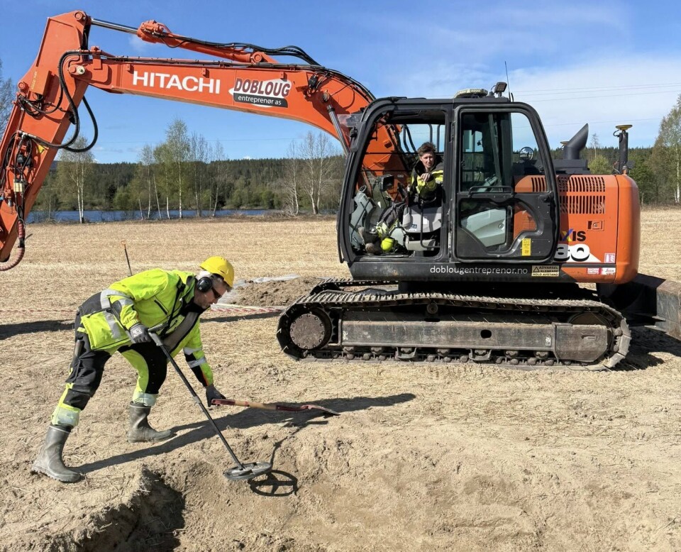A field with an excavator and an archaeologist holding a metal detector.
