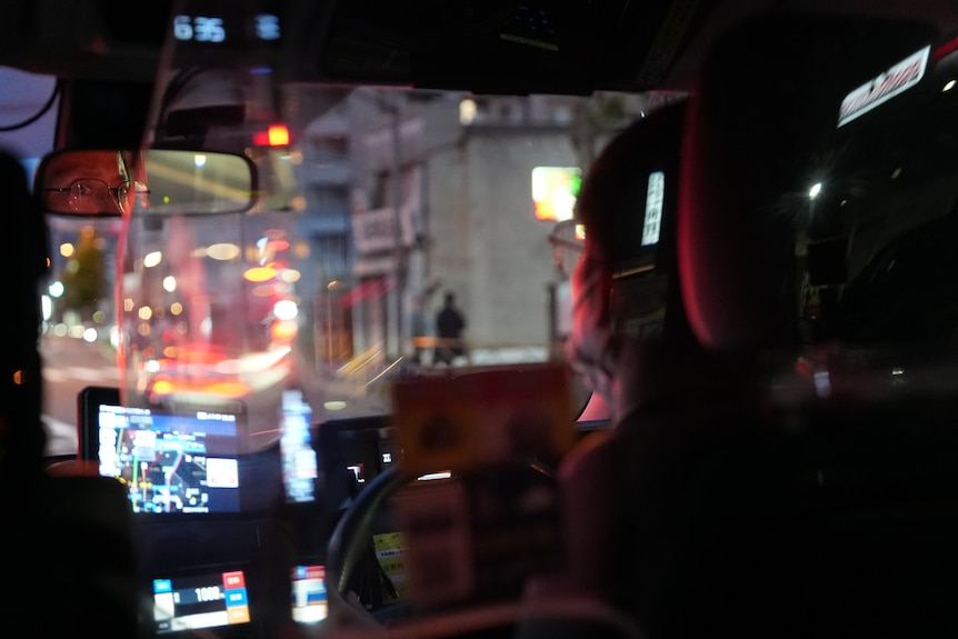 A close up of the driver's seat of a taxi with a man looking in the mirror.