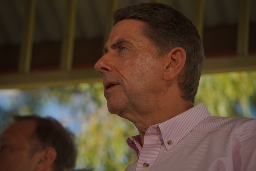 Low-angle shot of a man in a pink shirt speaking to left of frame.